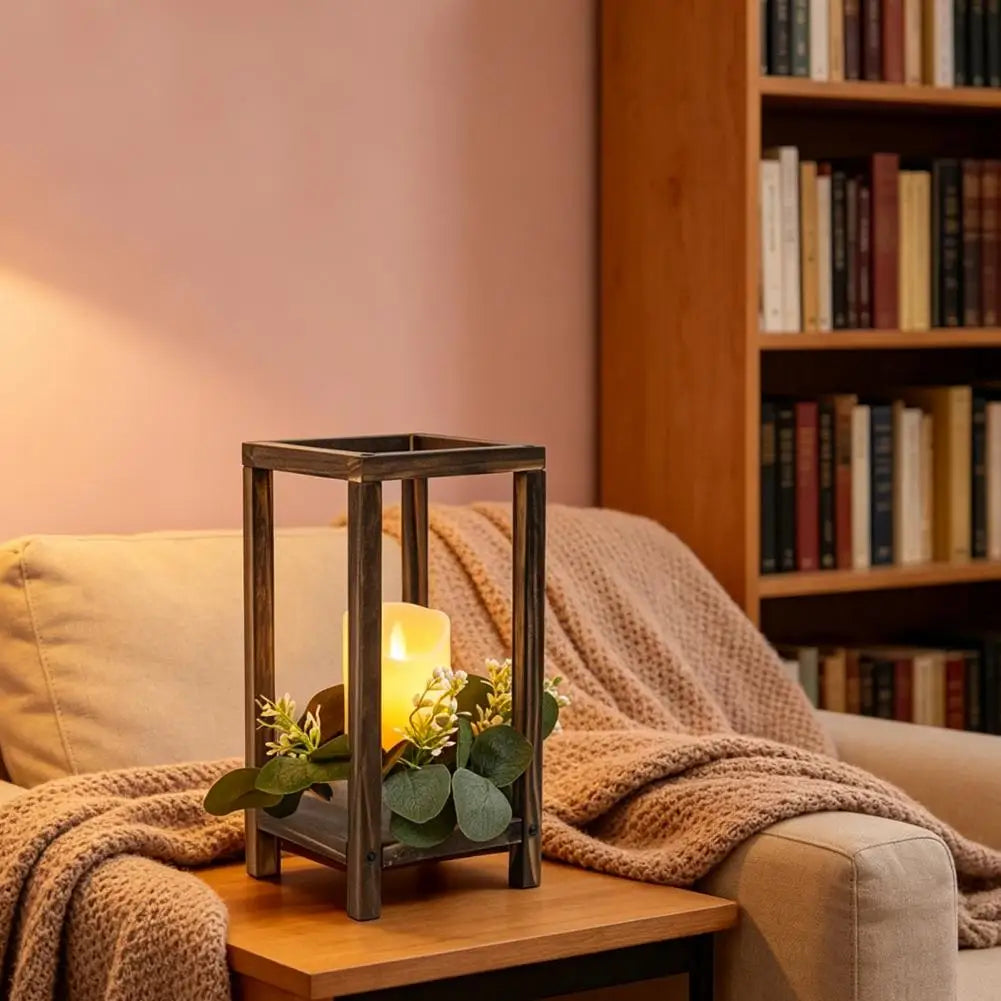 A rustic wooden candle holder lantern sits on a wooden surface next to a cozy knitted blanket and a bookshelf.