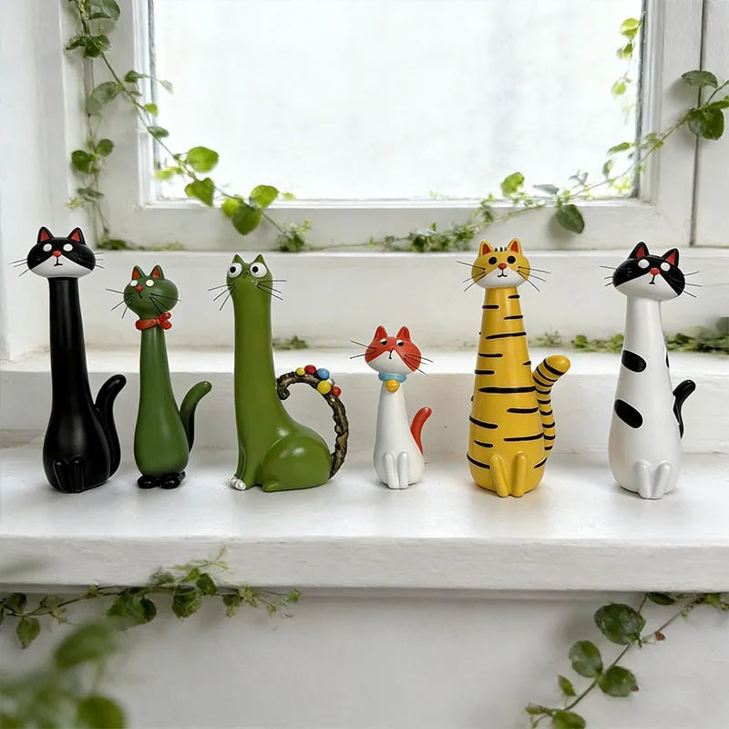 A collection of cat-shaped resin vases in various colors, including black, green, orange, and white, displayed on a windowsil