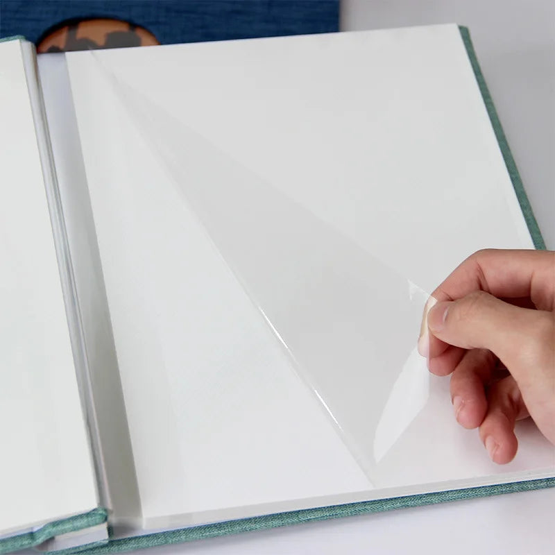 A hand is pressing a clear sheet of linen front scrapbook memory book onto a white page.