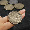 Una mano sostiene una moneda metálica conmemorativa dorada que presenta un ojo estilizado y la palabra SÍ.