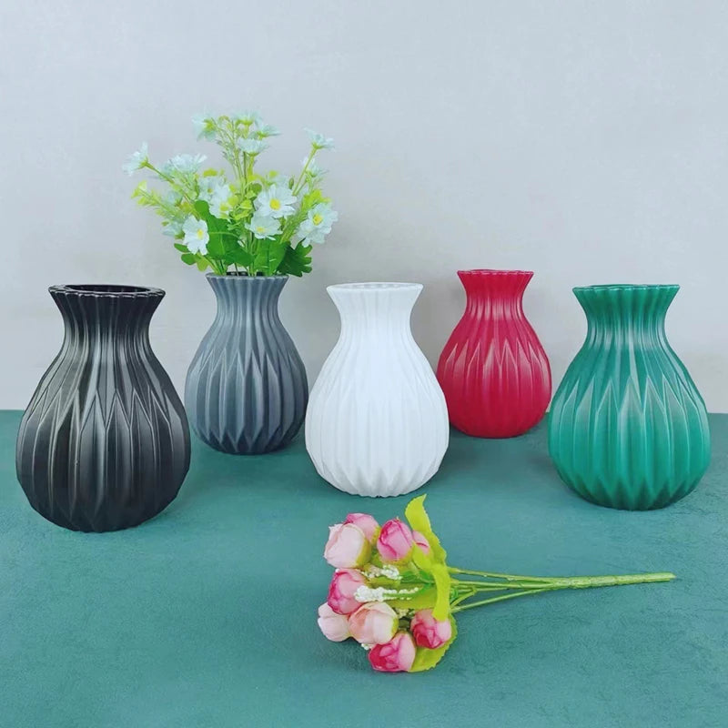 A collection of six Nordic style ceramic flower vases in various shades of gray, white, pink, and green on a teal surface.