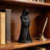 Schwarze Harzfigur einer befassten Gestalt, die den Toten darstellt, steht auf einem Holzregal neben alten Büchern und einem 