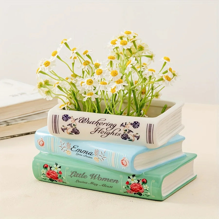 Un vase en céramique blanc en forme de livre, rempli de fleurs sauvages jaunes et blanches, repose sur une pile de trois livr