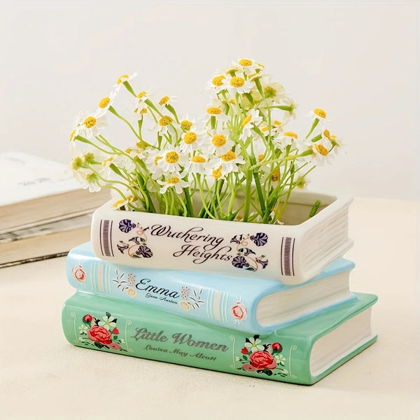 Un vase en céramique blanc en forme de livre, rempli de fleurs sauvages jaunes et blanches, repose sur une pile de trois livr