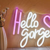 A glowing white neon sign spelling Hello Gorgeous mounted on a textured wall.