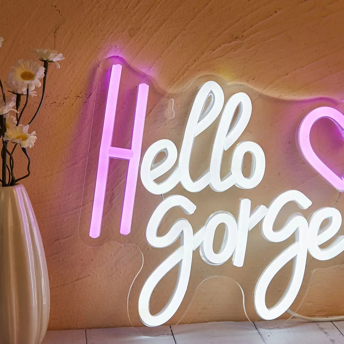 A glowing white neon sign spelling Hello Gorgeous mounted on a textured wall.