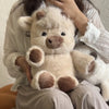 Une personne tient un jouet en peluche de veau écossais moelleux, beige clair, contre sa poitrine.