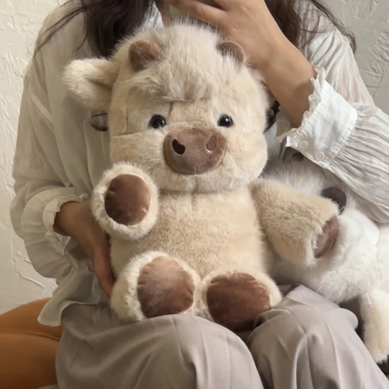Une personne tient un jouet en peluche de veau écossais moelleux, beige clair, contre sa poitrine.