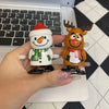 Two clockwork wind-up figurines, one a smiling snowman and the other a reindeer, are held against a black and white backgroun