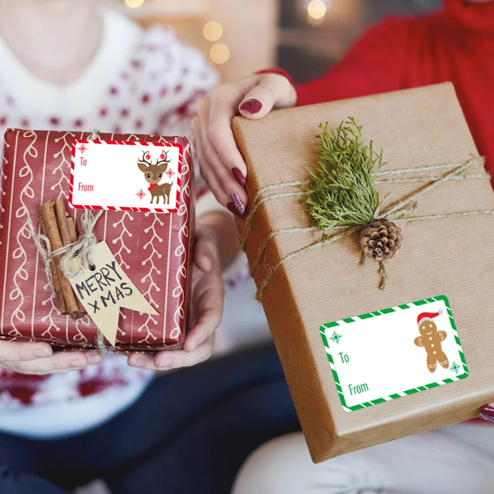 A person is holding a brown gift box tied with twine and green foliage, alongside a red gift box decorated with Christmas tag