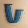 A vertical blue and green macrame wall tapestry hanging on a beige wall.