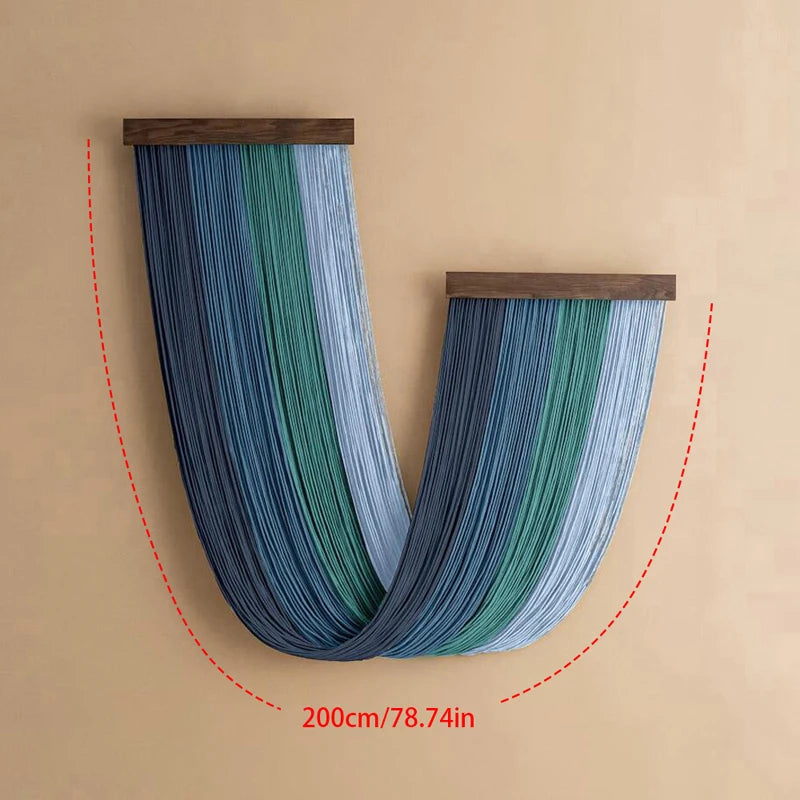 A vertical blue and green macrame wall tapestry hanging on a beige wall.