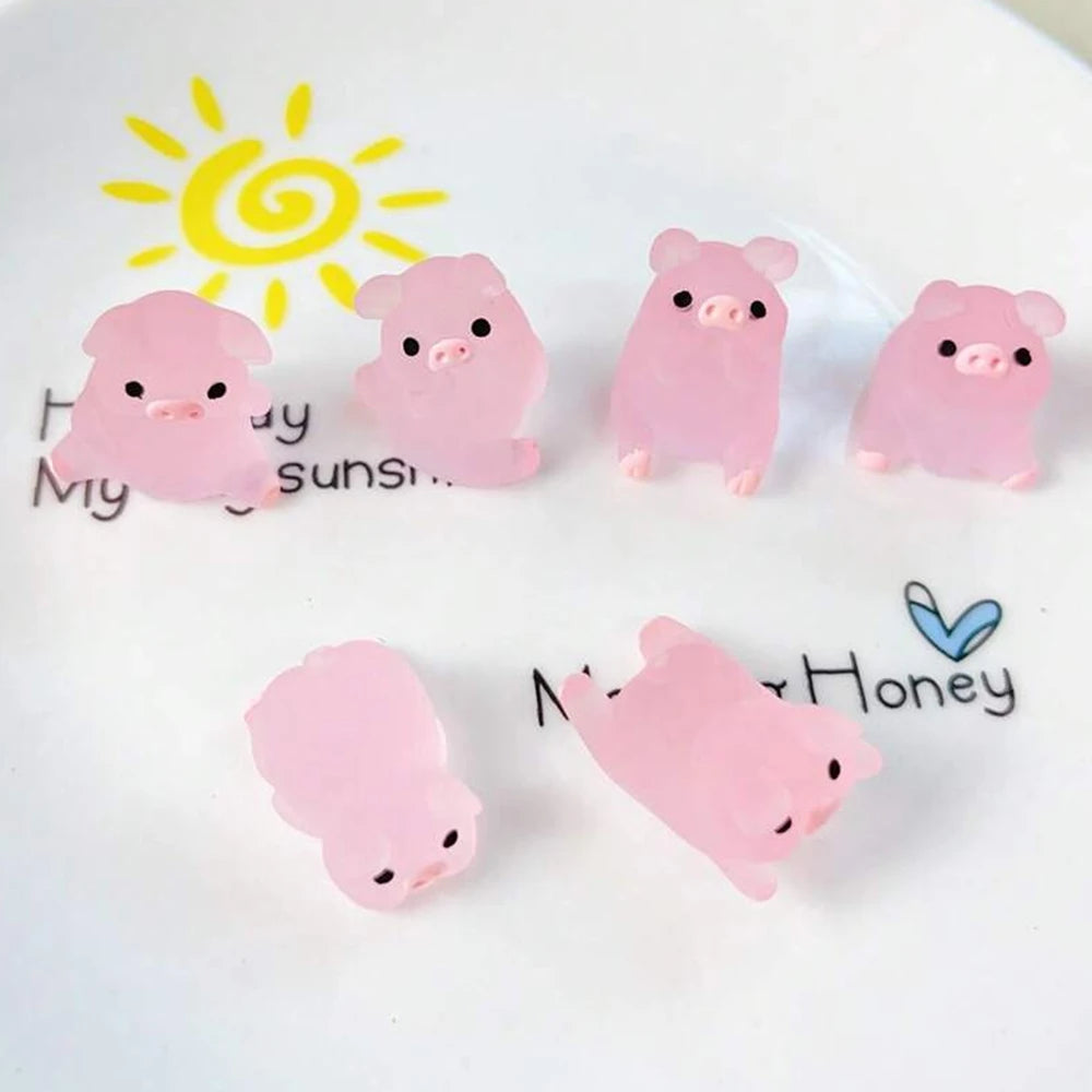 Pink glow-in-the-dark resin pig decorations arranged on a white surface with a yellow sun graphic.