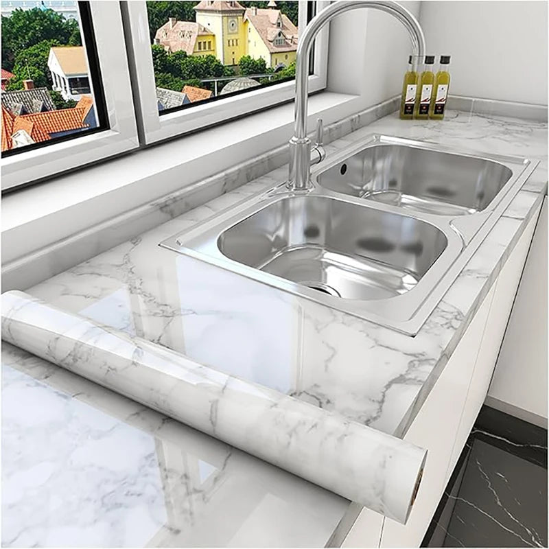 A stainless steel kitchen sink and faucet installed in a white marble countertop with a marble roll visible.