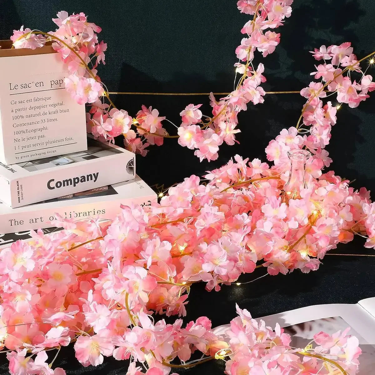 Pink cherry blossom string lights garland draped over a wooden box and book.