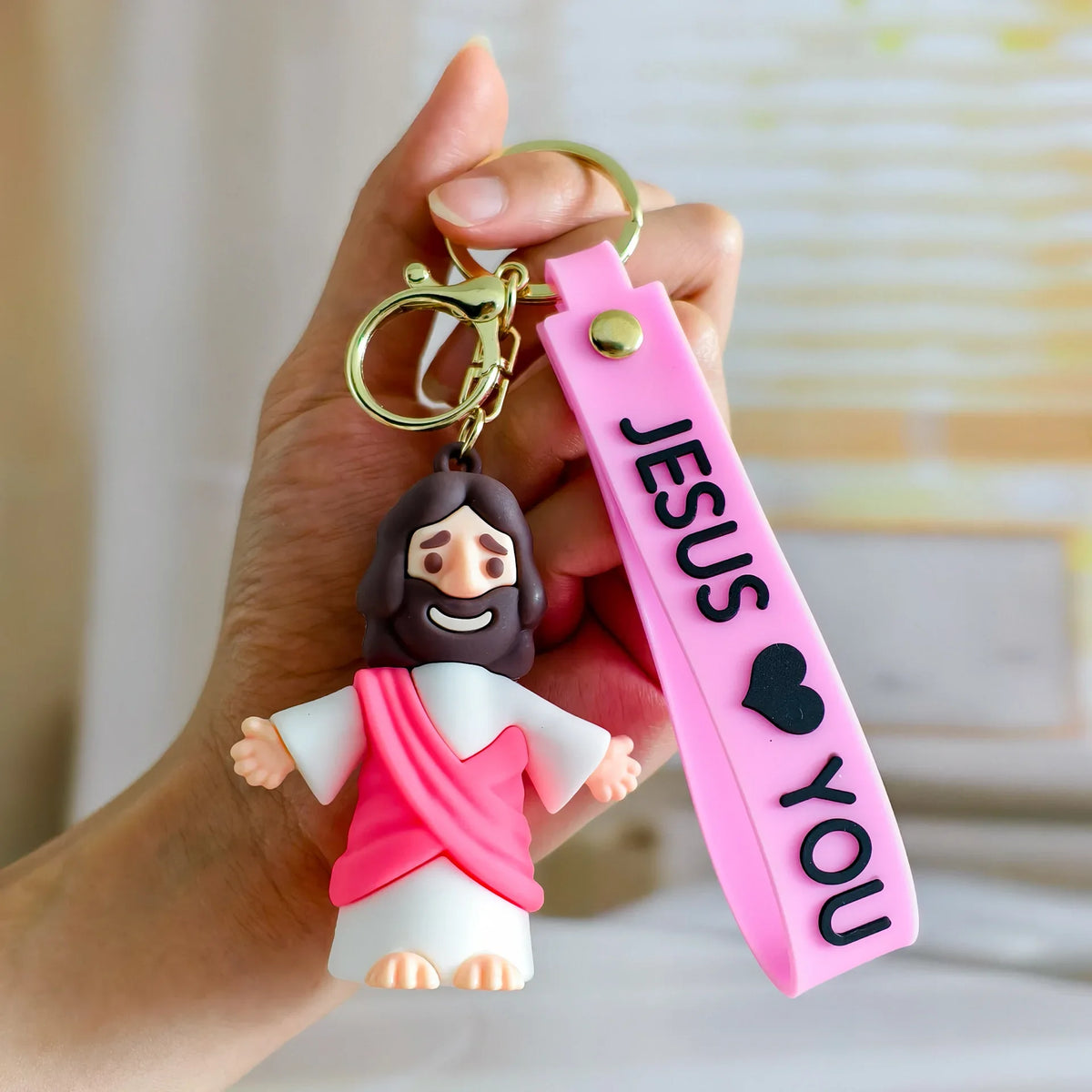 A hand holds a silicone keychain featuring a Jesus figure and a pink strap engraved with the words Jesus you