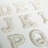 White rhinestone alphabet letters D, E, K, J, and P scattered on a white background.