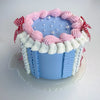 A round light blue cake decorated with pink frosting swirls and white piping, topped with small pearl accents.