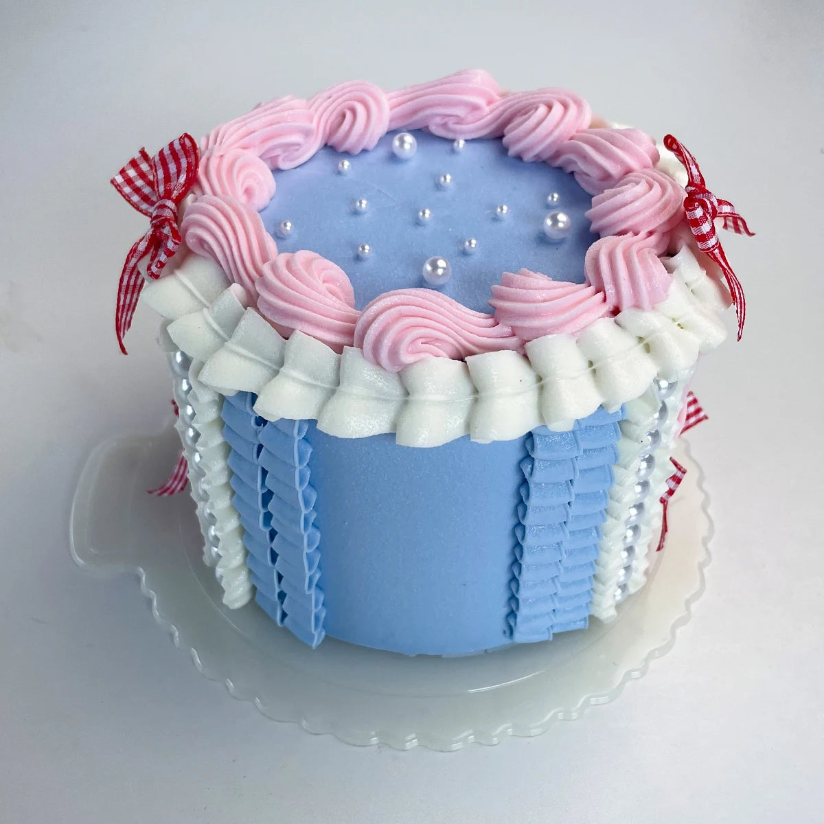A round light blue cake decorated with pink frosting swirls and white piping, topped with small pearl accents.