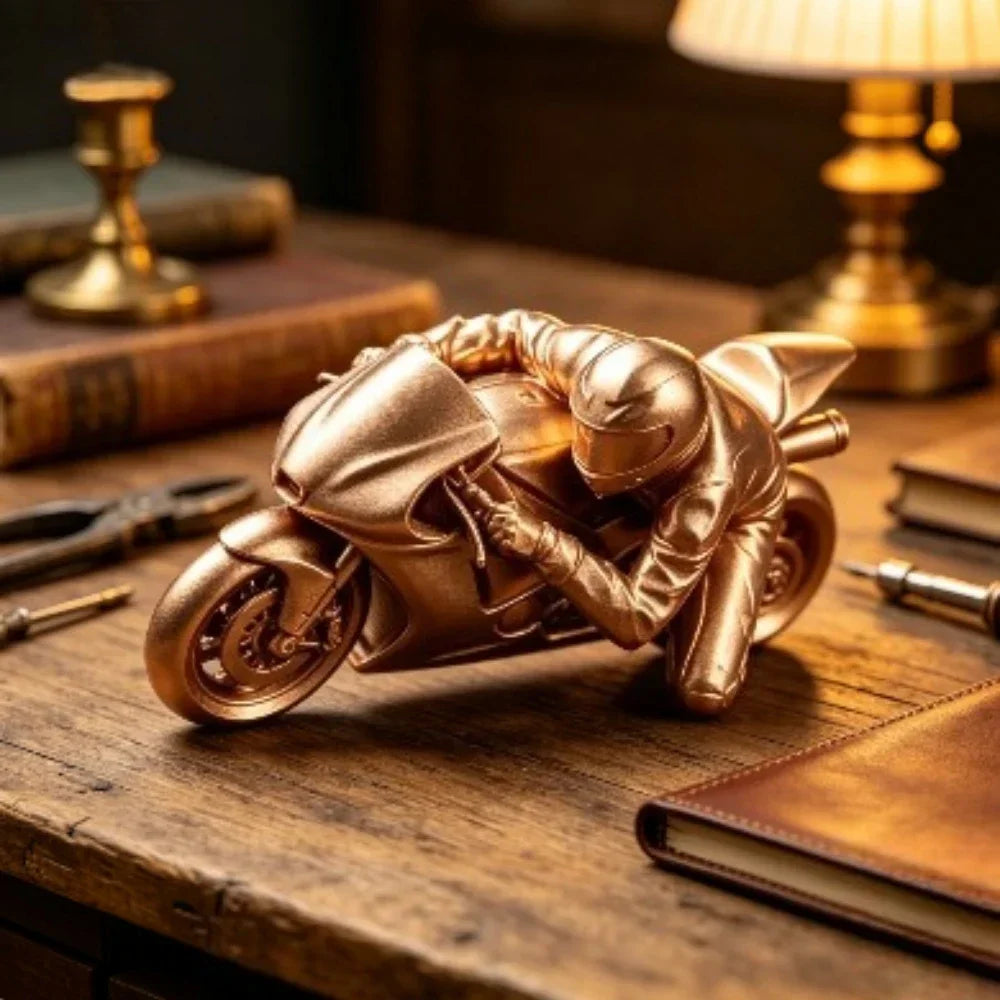 A bronze-colored 3D printed figurine of a racing motorcycle rider placed on a wooden desk with books and tools.