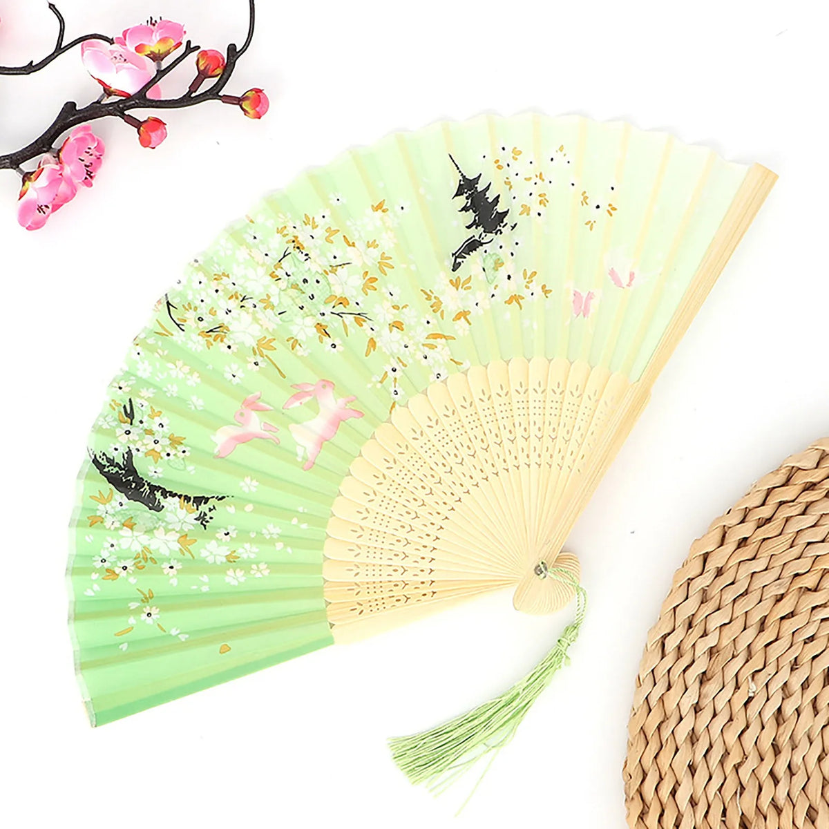 A light green vintage bamboo folding fan with pink and black designs, shown partially open.