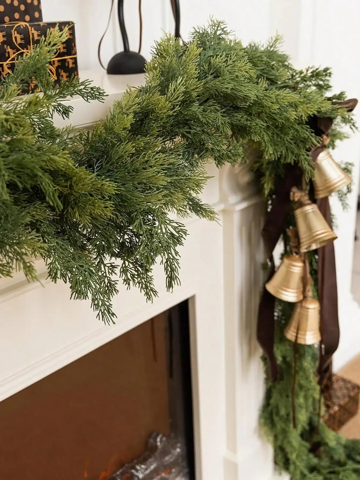 A long garland of artificial Norfolk pine greenery in winter green hangs over a white fireplace mantel.