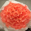 A bouquet of vibrant coral pink silk roses wrapped in sheer white tissue paper.