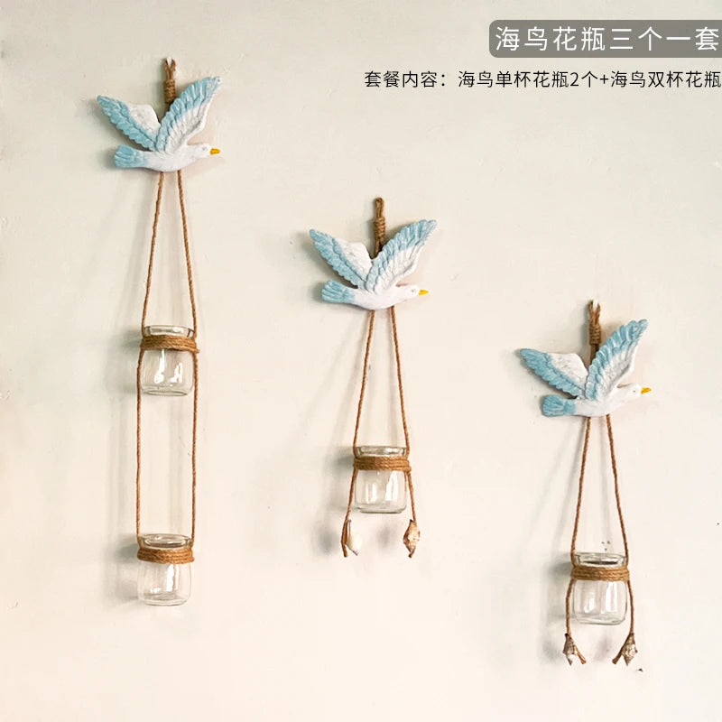 Three decorative glass terrariums featuring white and blue seagull-like flowers hanging by twine.