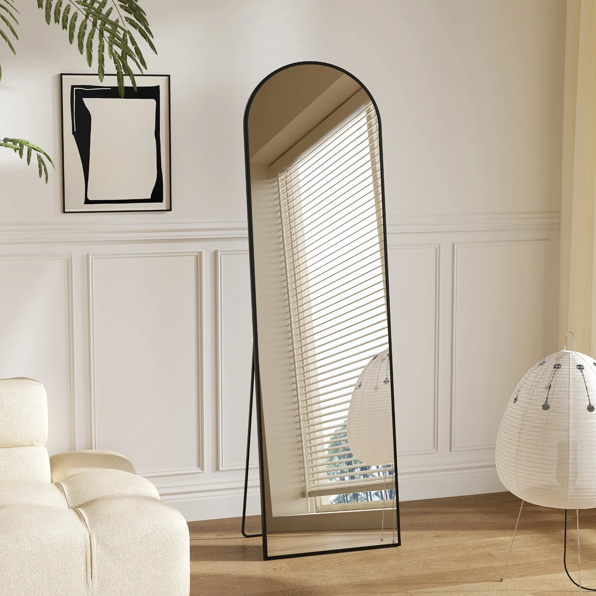 A full length floor mirror with an aluminum frame and vertical blinds leaning against a white wall.