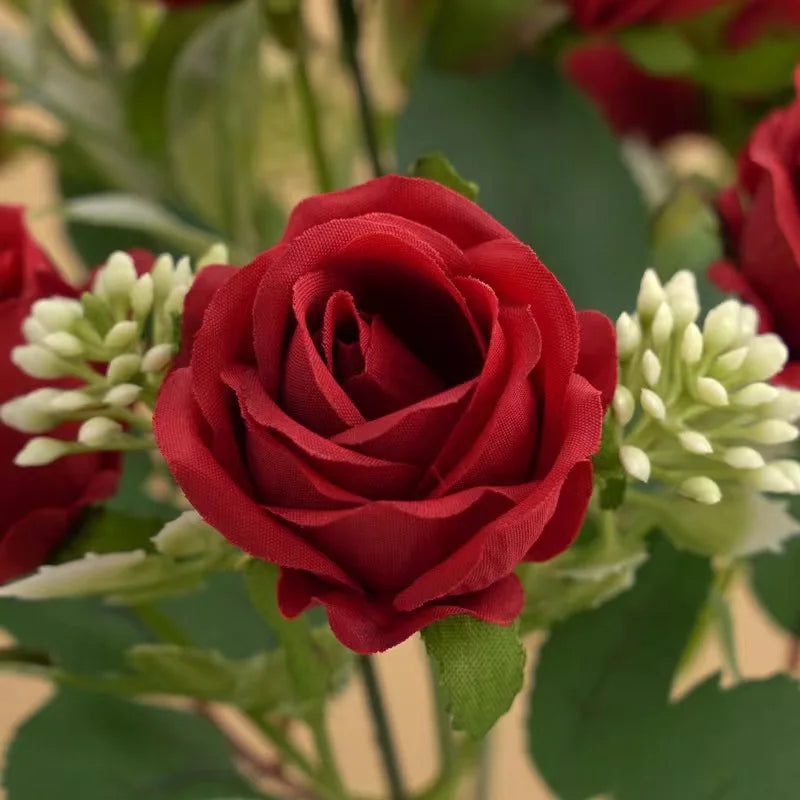 A deep red artificial rose flower with green leaves and white buds on a stem.