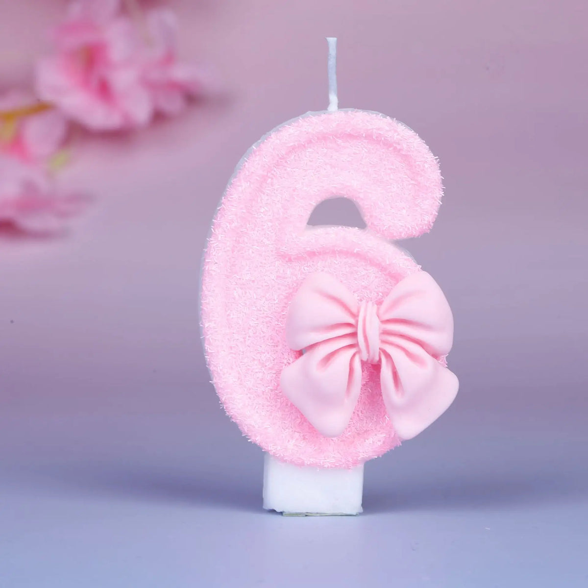 Glittery pink number six birthday candle with a decorative pink bow