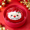 A red Christmas squishy stress reliever shaped like Santa Claus with a white beard and red nose, resting in a pink container.