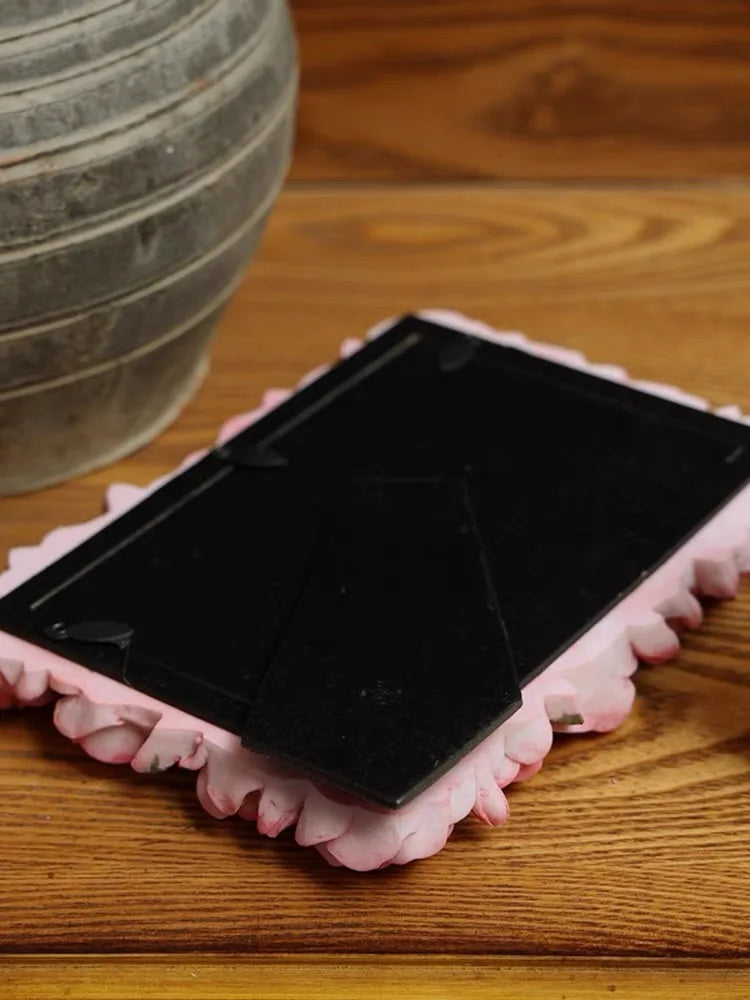 A black resin picture frame shaped like a pink rose is displayed on a wooden surface.