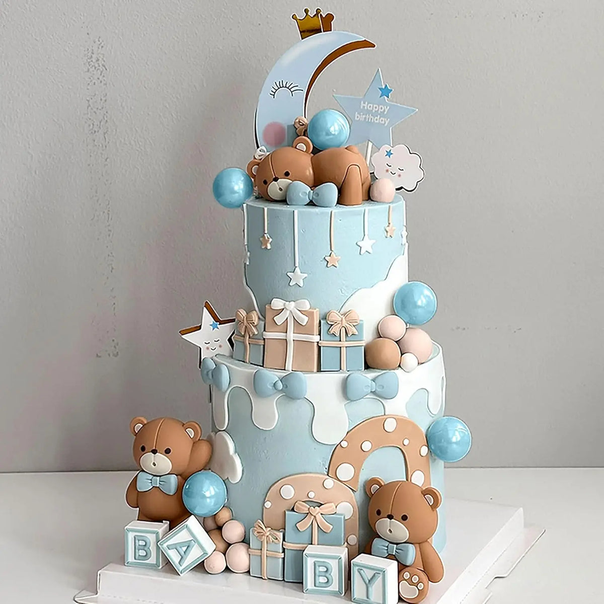A tiered blue cake decorated with teddy bears, stars, clouds, and blue balls for a baby shower.