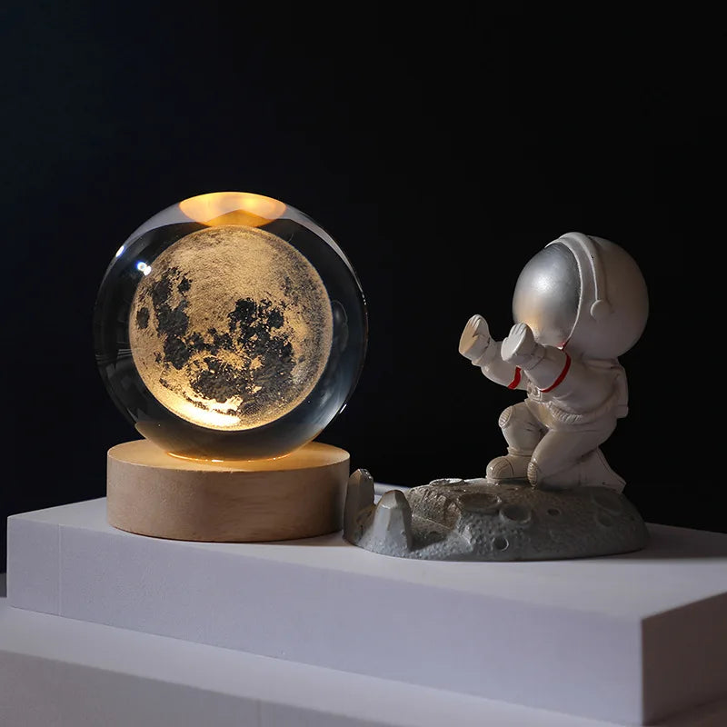 Galaxy crystal ball night light featuring a moon inside on a wooden base and a small statue.