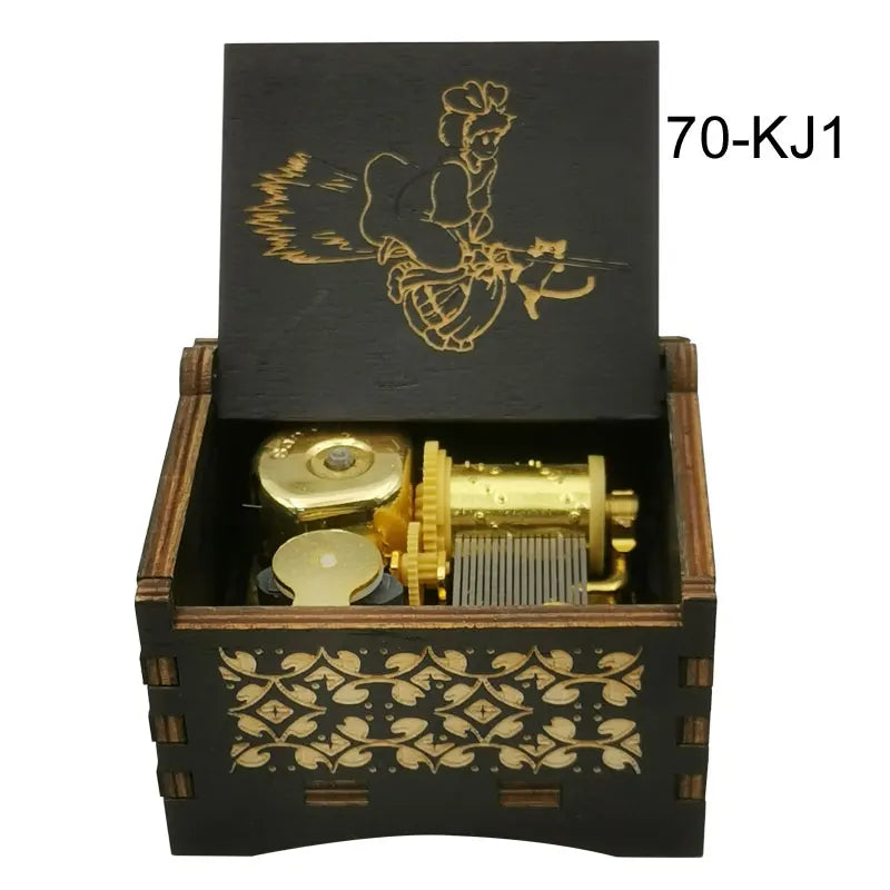 A black wooden music box with a lid featuring a gold-colored anime character and an open compartment containing a brass cylin