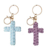 A pair of bohemian woven cross keychains, one light blue and one purple, with gold-toned rings.