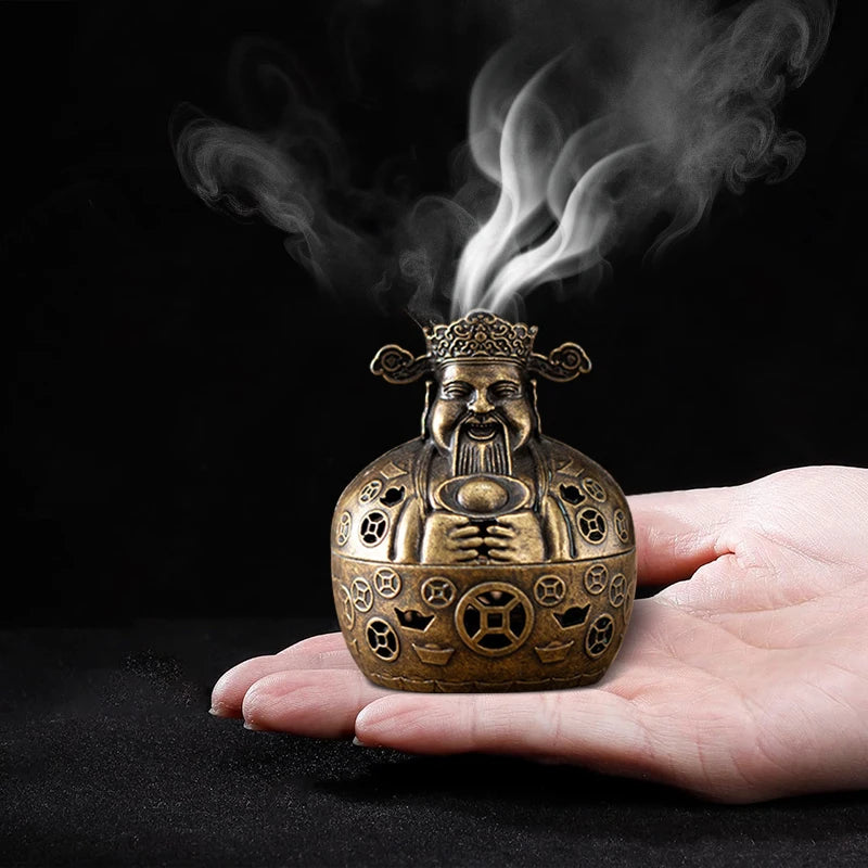 A hand holds a vintage brass incense burner with smoke rising from it against a dark background.