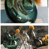 A set of three clear glass mini vases with stems and leaves arranged on a white surface.