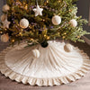A festive green Christmas tree decorated with ornaments and lights, resting on a velvet skirt with a ruffled edge.