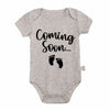 A light gray baby bodysuit with black text that reads Coming Soon