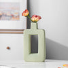 A light green geometric ceramic vase holding two pink roses on a white surface.