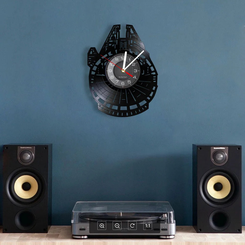 A black vinyl record wall clock is displayed above a wooden surface with two speakers.