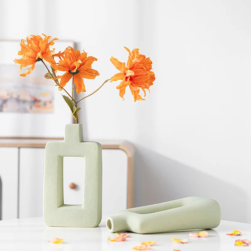 An orange flower arrangement in a light green geometric ceramic vase on a white table.