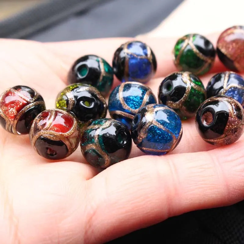 A hand holds a collection of handcrafted lampwork glass beads with gold accents in various colors and shades.