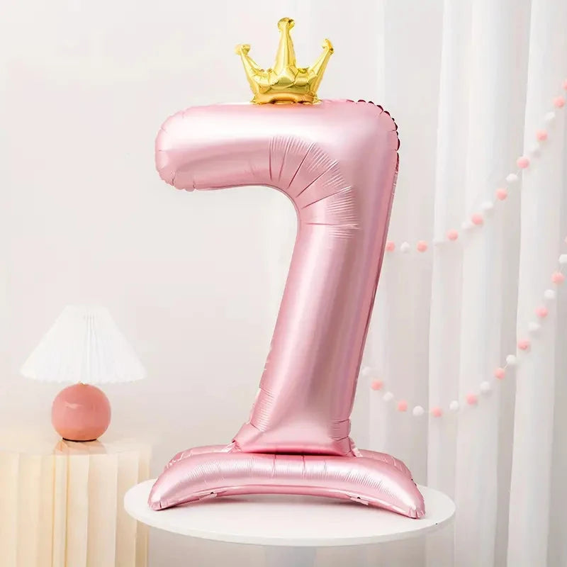 A pink foil number balloon shaped like the number one with a gold crown on top