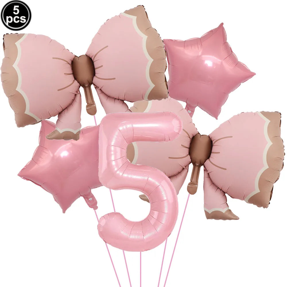 A set of pink bow disposable party tableware, including a large number five balloon and several pink balloons.