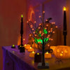 A glowing Halloween birch tree lamp with LED lights sits on a table surrounded by orange candles.