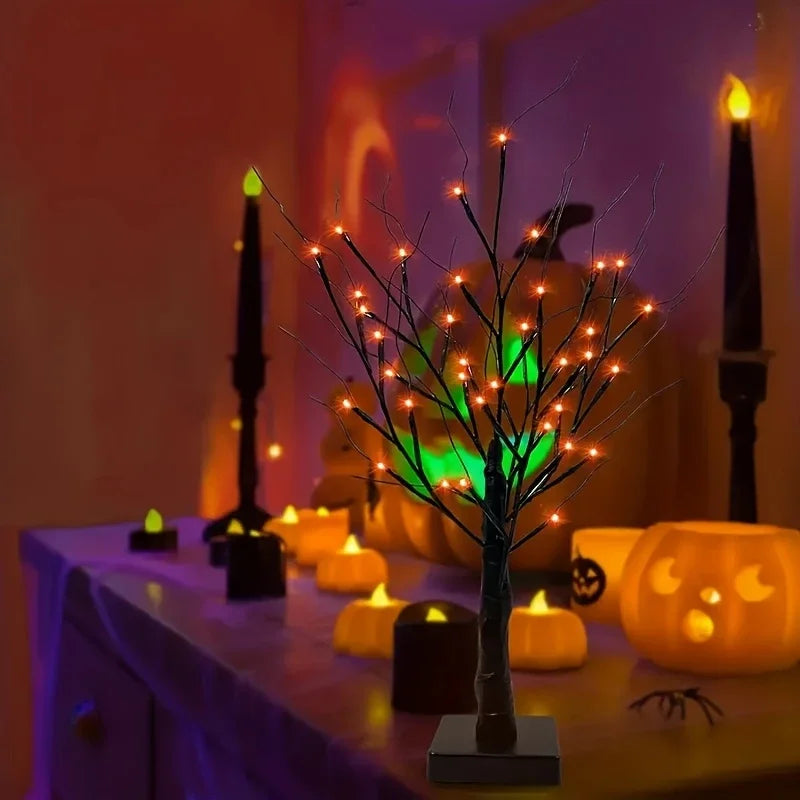 A glowing Halloween birch tree lamp with LED lights sits on a table surrounded by orange candles.
