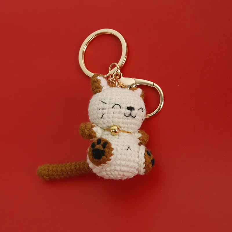 A handcrafted crochet cat keychain pendant with a white and brown textured body and ears, attached to a gold-colored ring.